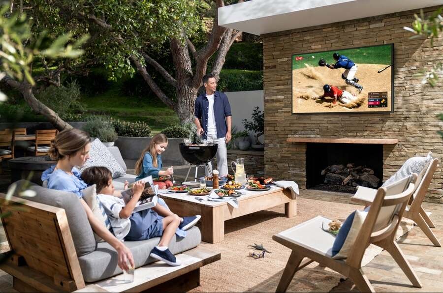 A family watches a baseball game on their Terrace outdoor TV while having a cookout.