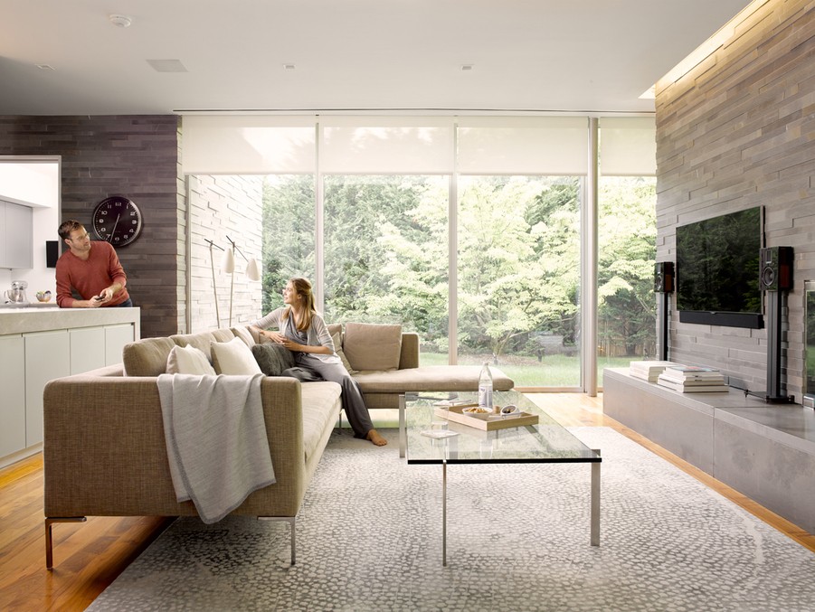 couple talks in living room with floor to ceiling windows featuring partially raised roller shades