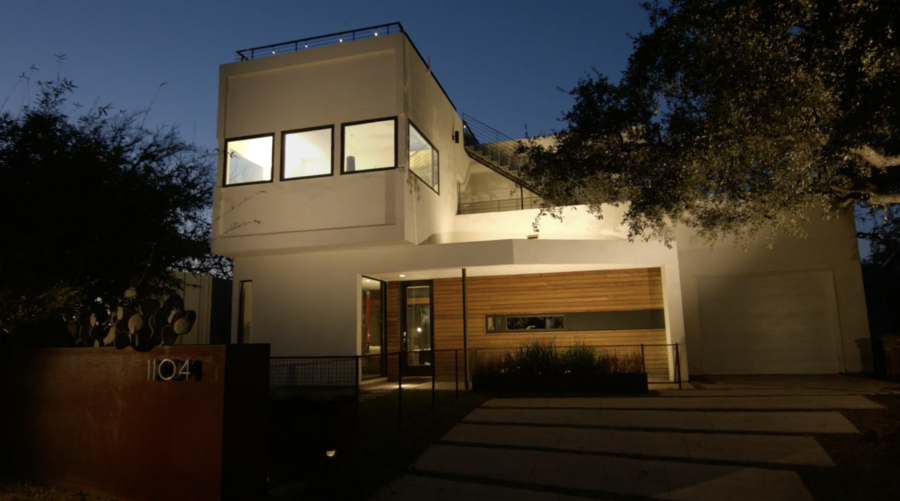 A modern two-story house in the evening, illuminated by indoor and outdoor lights.