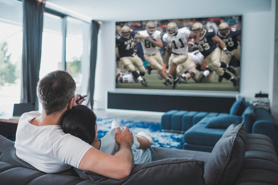 A couple watches a football game on a large-screen TV in a modern Houston home theater.