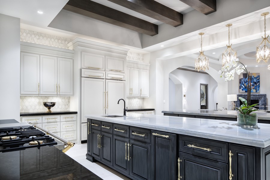 An elegant kitchen with dark cabinets, marble counters, and bright lighting.