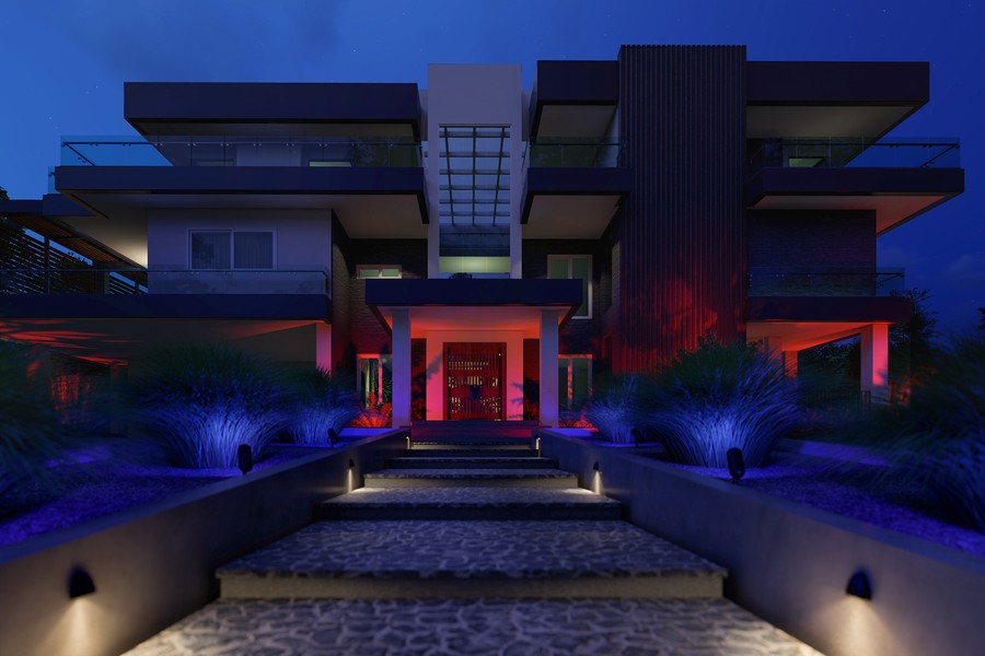 Ketra-ready Coastal Source lighting fixtures shine blue and red along landscaped hedges in a front yard.