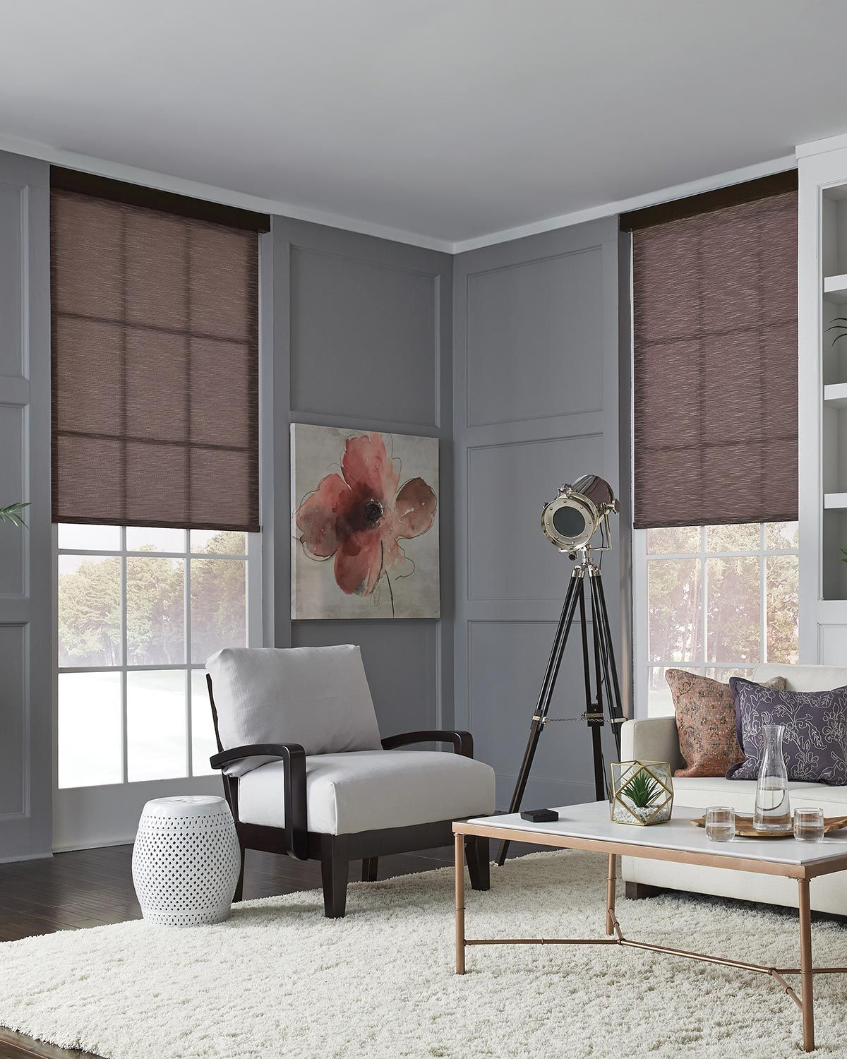 A stylish living room with gray paneled walls, featuring Lutron roller shades on the windows, complemented by modern furniture and decorative elements.